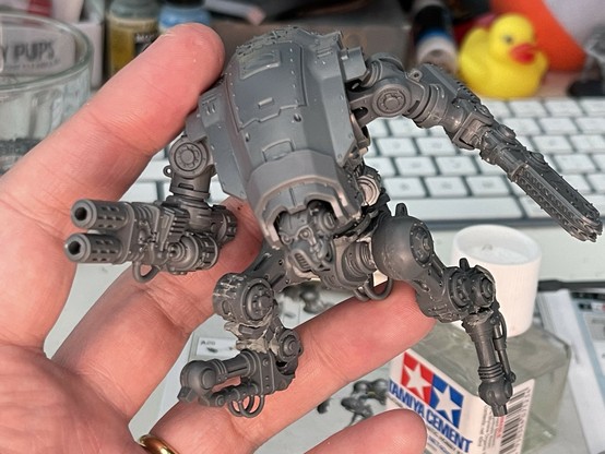 A partly-constructed Armiger Warglaive model from Warhammer held together with Blu Tack. The sword arm is held backwards and the thermal spear is aimed forwards. The legs are in a rough, running pose.